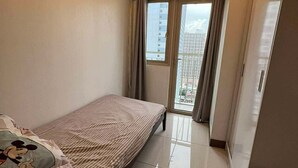 A small, tidy bedroom with a single bed, a window with curtains, and a view of a cityscape. - Bayfront Cozy Stay at SMDC Coast Residences (Pasay City)