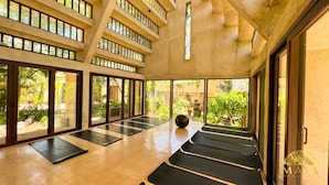 Een ruime yogastudio met grote ramen, houten vloeren en zwarte yogamatten in rijen.