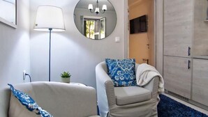 A modern living room with a sofa, a chair with a patterned cushion, a floor lamp, a small potted plant, and a wardrobe. - Indigo Apartment by Corfuescapes  (Corfu)