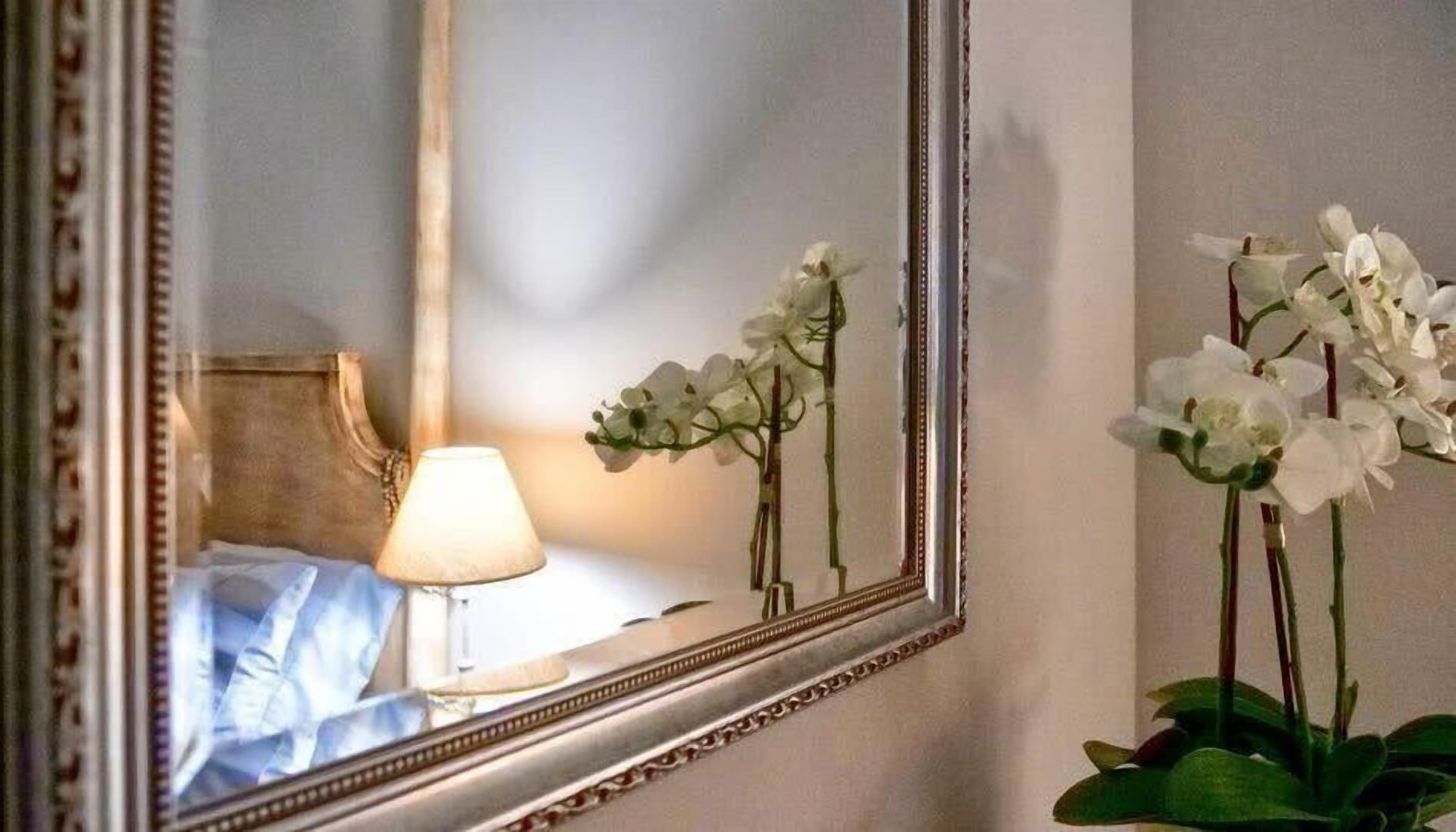 A mirror reflecting a bed, a lamp, and white orchids.