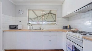 Una cocina compacta con armarios blancos, un microondas, un fregadero, una estufa y una ventana con vistas a una edificación exterior.