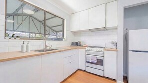 A kitchen with white cabinets, a stainless steel sink, a stove, and a refrigerator.