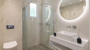 Un bagno moderno con doccia vetro, lavandino bianco e dispenser per sapone nero, e uno specchio rotondo a parete.
