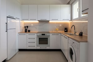 A modern kitchen with white cabinets, a built-in oven, a dishwasher, and a washing machine. - Island Hills- Sunshine, Apartment (Rhodes)