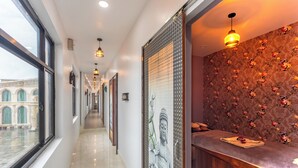A hotel corridor with a view of a courtyard, a statue, and a reception area with a patterned wall and a counter. -  Lords Riverside Resort Muduba - A Wellness Nature Retreat (Tirthalli)