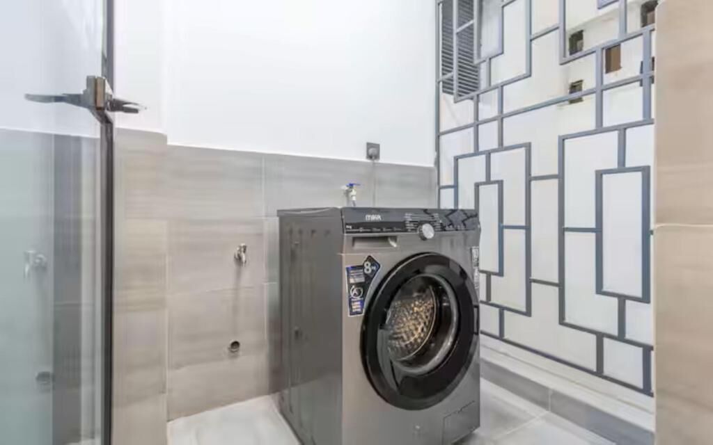 Uma casa de banho moderna com máquina de lavar embutida, cabine de duche em vidro e design geométrico na parede.