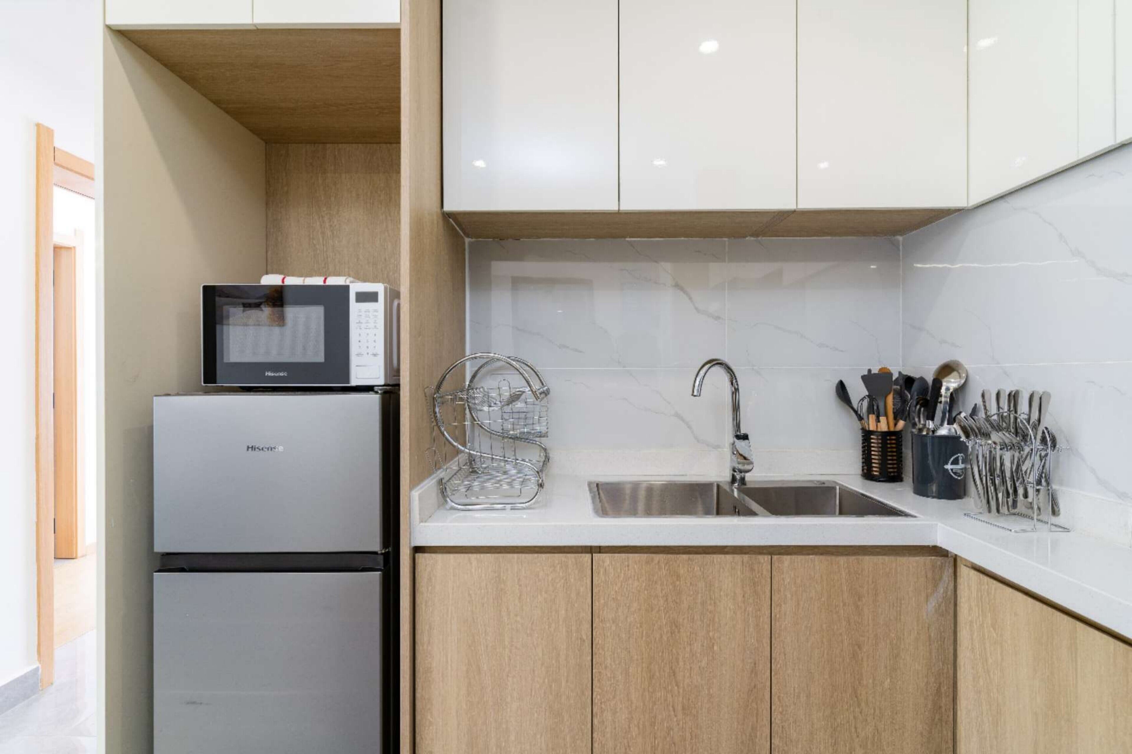 Une cuisine de taille réduite, équipée d’un four à micro-ondes, d’un évier et de meubles de rangement en bois.