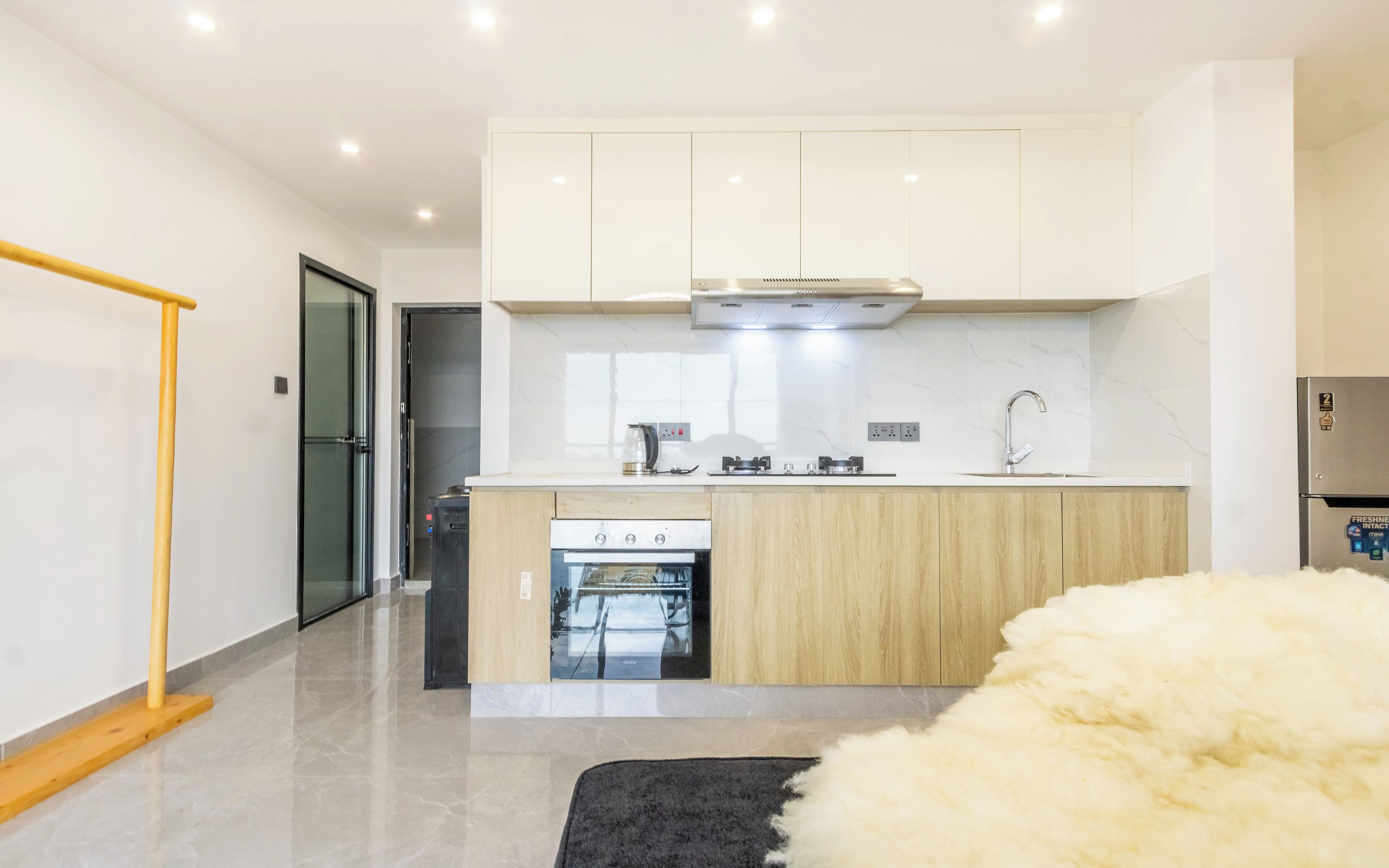 A modern kitchen with a built-in oven, a stainless steel refrigerator, and a black and white rug.