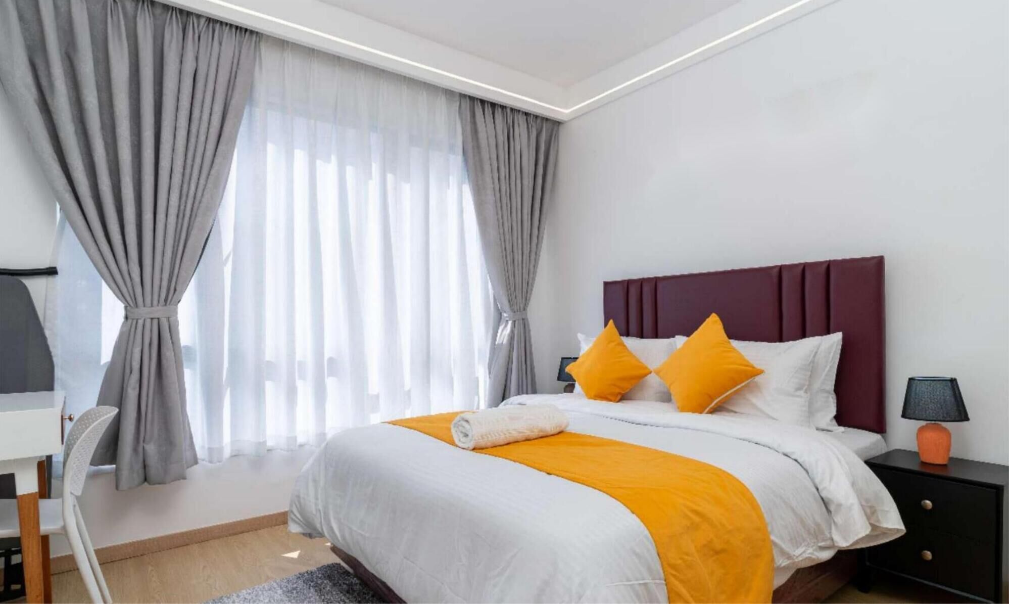 Une chambre d’hôtel moderne avec un grand lit, des rideaux gris, une table de chevet en bois et un bureau.