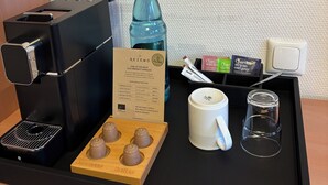 Uma estação de café com cafeteira, garrafa de água, guia de seleção de cápsulas de café, caneca e copo.