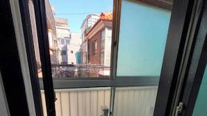 Un balcon étroit doté d’une rambarde en métal, d’un petit climatiseur et offrant une vue sur les immeubles voisins.