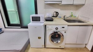 Une petite cuisine équipée d’un four à micro-ondes, d’un grille-pain, d’un évier et d’un lave-linge.