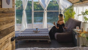 A cozy room with a large window, a bed, a couch, and a small table with a lamp and a plant. - Nubdao Glamping (Kanchanaburi)