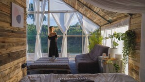 A room with a large window, a bed, a sofa, and a chandelier. - Nubdao Glamping (Kanchanaburi)