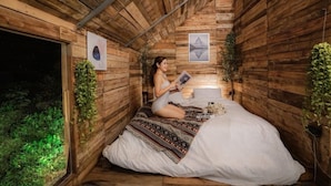 A cozy, wooden cabin-style room with a bed, a reading lamp, and framed pictures on the walls. - Nubdao Glamping (Kanchanaburi)