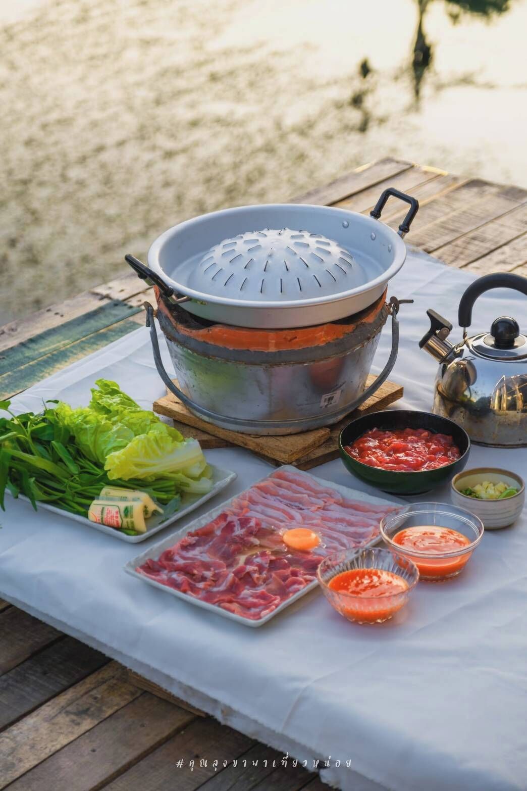 Un equipo de cocina portátil con una vaporera, una tetera y diversos alimentos sobre una mesa.