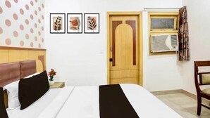 A hotel room with a bed, a wooden door, an air conditioning unit, and a chair. - LE ALFANSO BY AZAD RAM (New Delhi)