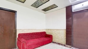 A red sofa in a room with a tiled floor, a wooden door, and a brown wall. - LE ALFANSO BY AZAD RAM (New Delhi)