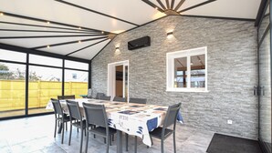 Un comedor con una mesa dispuesta para seis personas, rodeada de sillas, en una habitación con pared de piedra y ventanas amplias.