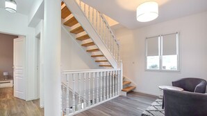 Un interior moderno con una escalera de madera, paredes blancas y un ventanal grande.