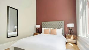 A neatly made bed with a tufted headboard, two bedside lamps, and a bedside table with a decorative item. - Two Stylish Suites + Full Kitchen | Canal St + Quarter | The Harlequin (New Orleans)