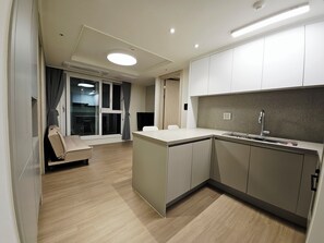 Et moderne køkken med en indbygget ø, et spiseområde med en sofa, og en stor skydedør, der fører ud til en balkon.