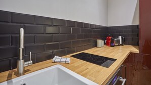 Une cuisine moderne avec un dosseret de carreaux noirs, un robinet en acier inoxydable, un plan de travail en bois, une plaque de cuisson à induction intégrée, une machine à café et un grille-pain.