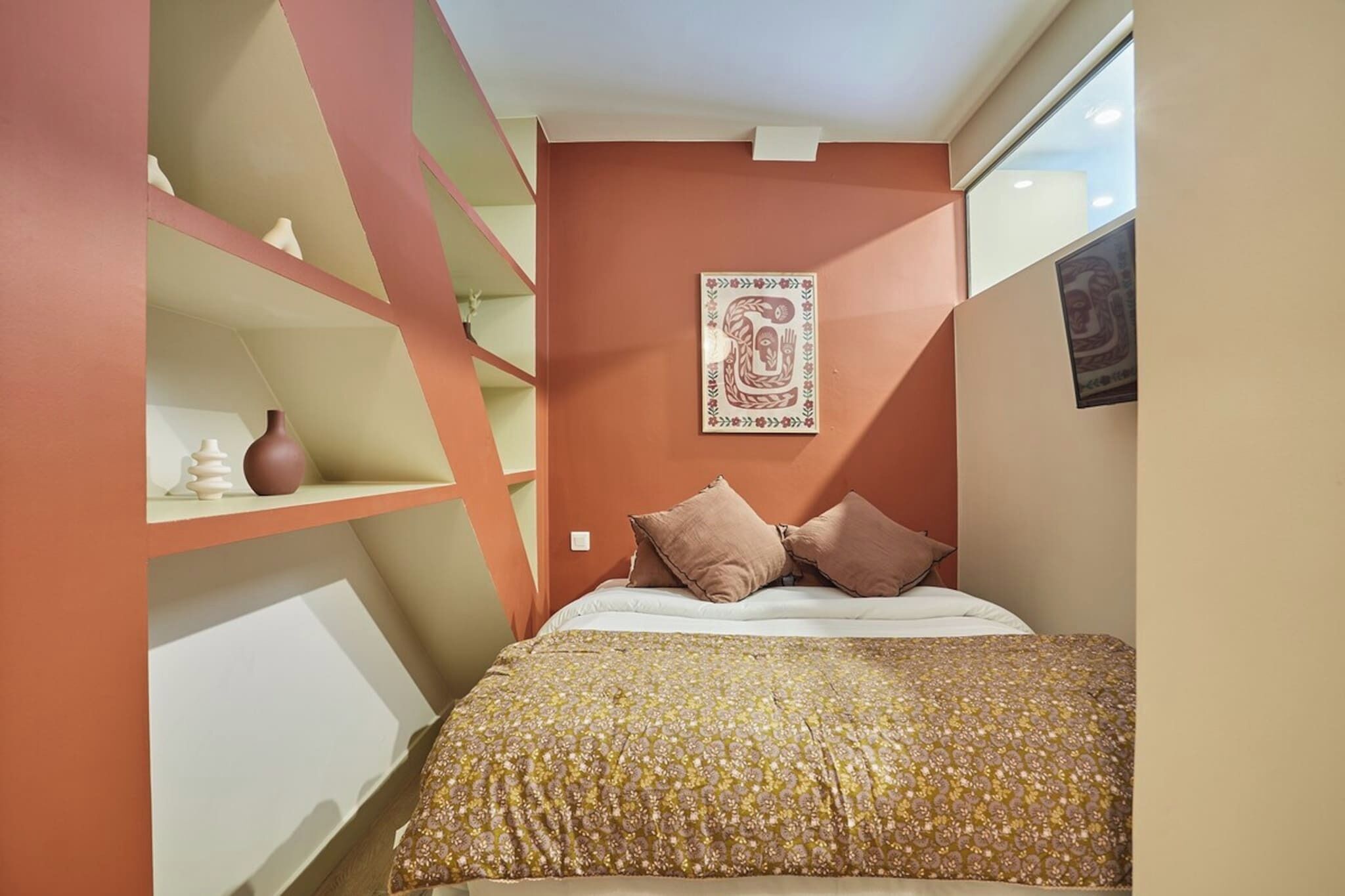 A bedroom with a bed, a shelf with decorative items, and a wall with a framed artwork.