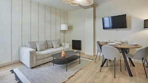 En moderne stue med sofa, sofabord og spiseområde med fire stole og et bord dækket til fire personer.