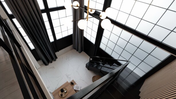 A modern interior with a staircase, a ceiling light fixture, and a view through a window with a grid pattern. - Koukaki Golden Lofts (Athens)