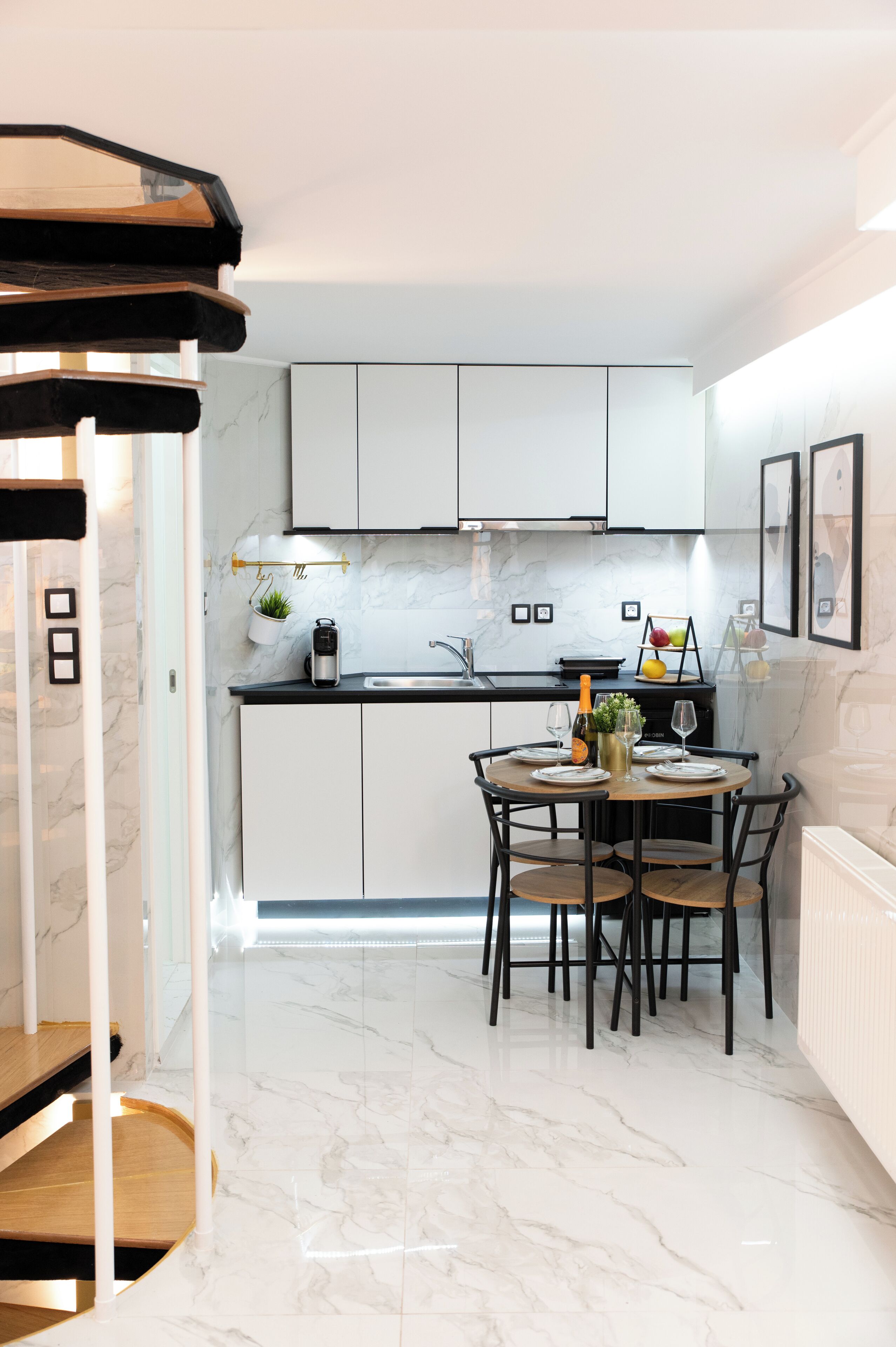 Une cuisine moderne avec des meubles blancs, un plan de travail en marbre et un coin repas avec une table dressée pour quatre personnes.