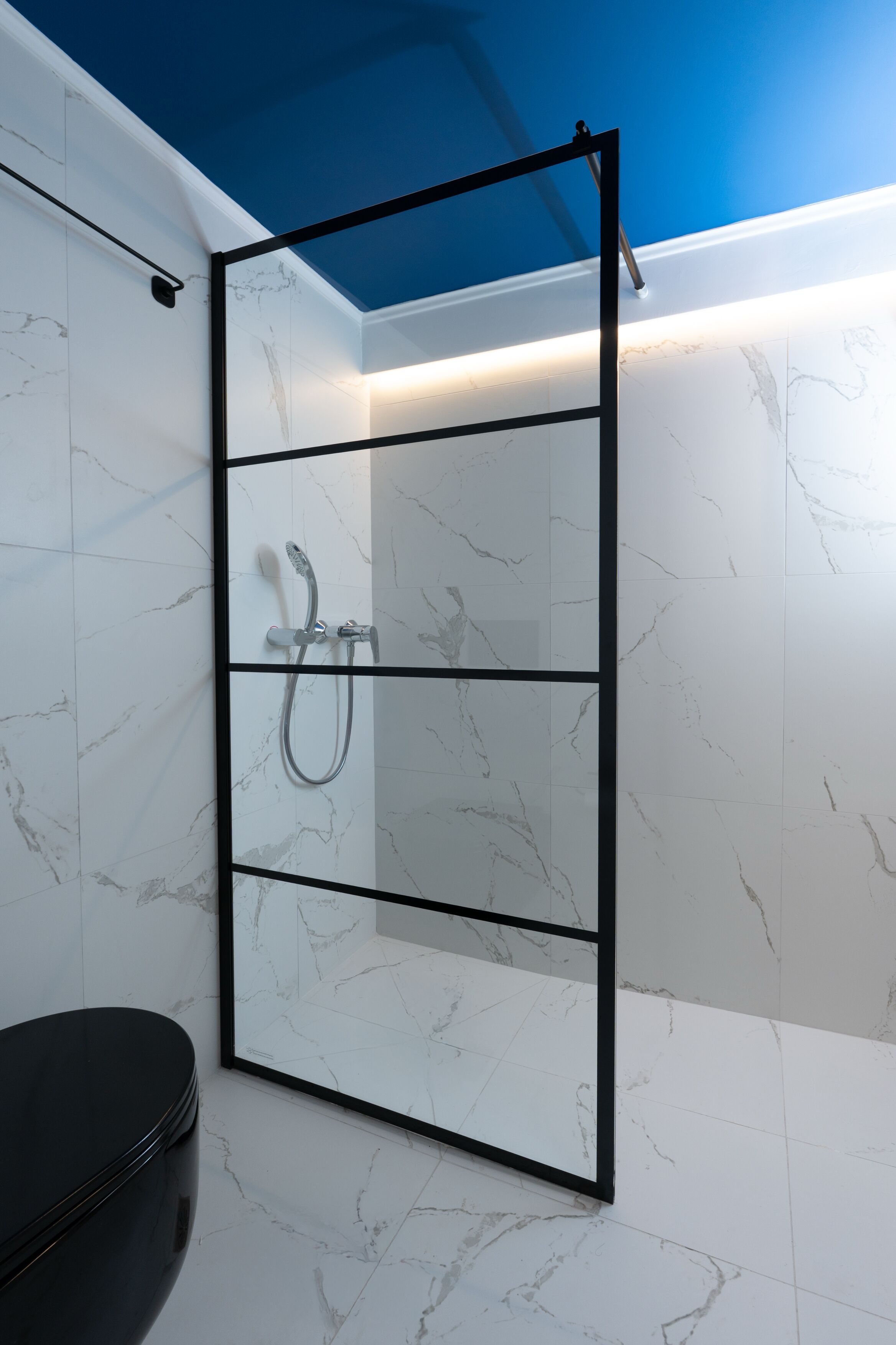 A modern bathroom with a glass shower enclosure, white marble tiles, and a black toilet.