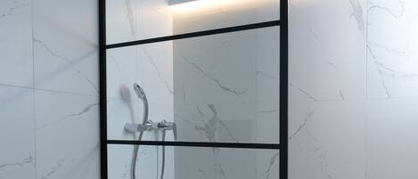 A modern bathroom with a glass shower enclosure, white marble tiles, and a black toilet.