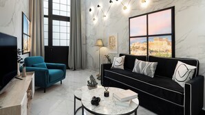 A modern living room with a black sofa, teal armchair, and a marble floor. - Koukaki Golden Lofts (Athens)