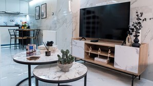 A modern living room with a marble floor, a wooden TV stand, a flat-screen TV, a dining area with a table and chairs, and a kitchen in the background. - Koukaki Golden Lofts (Athens)