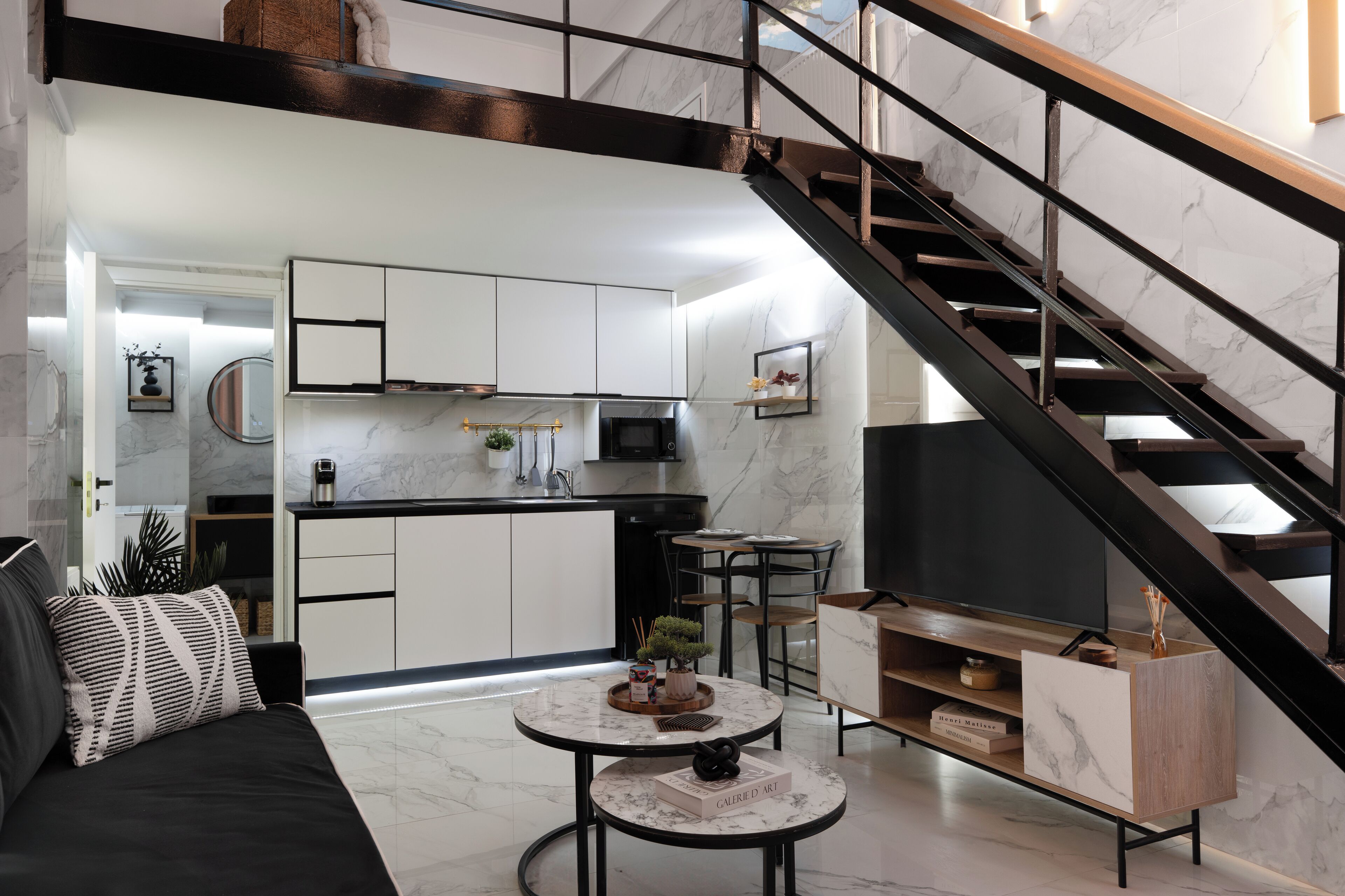 A modern living room with a black sofa, a round coffee table, and a staircase with a black railing.