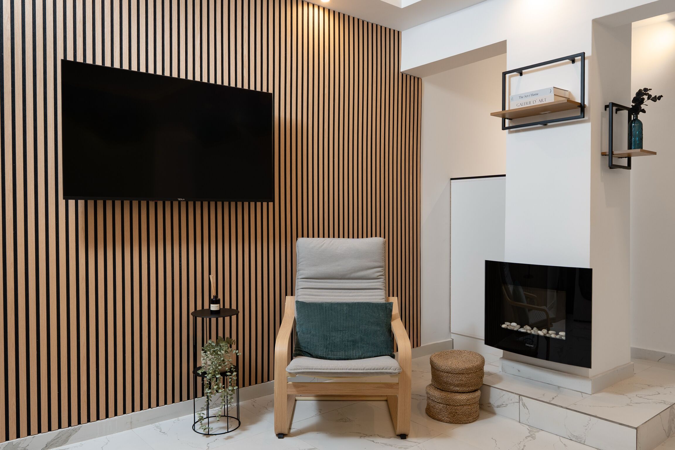 Ein modernes Wohnzimmer mit Flachbildfernseher, einer Wand aus Holzlatten, Kamin und einem bequemen Sessel mit Kissen.