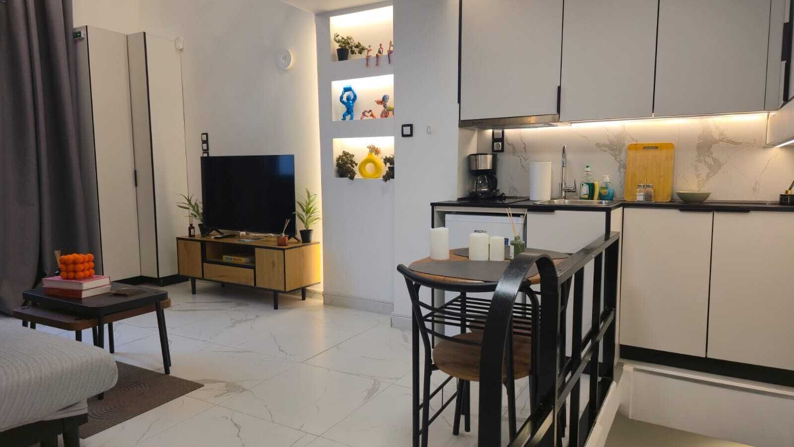 A modern kitchen with a dining area, a TV, and a small seating space.