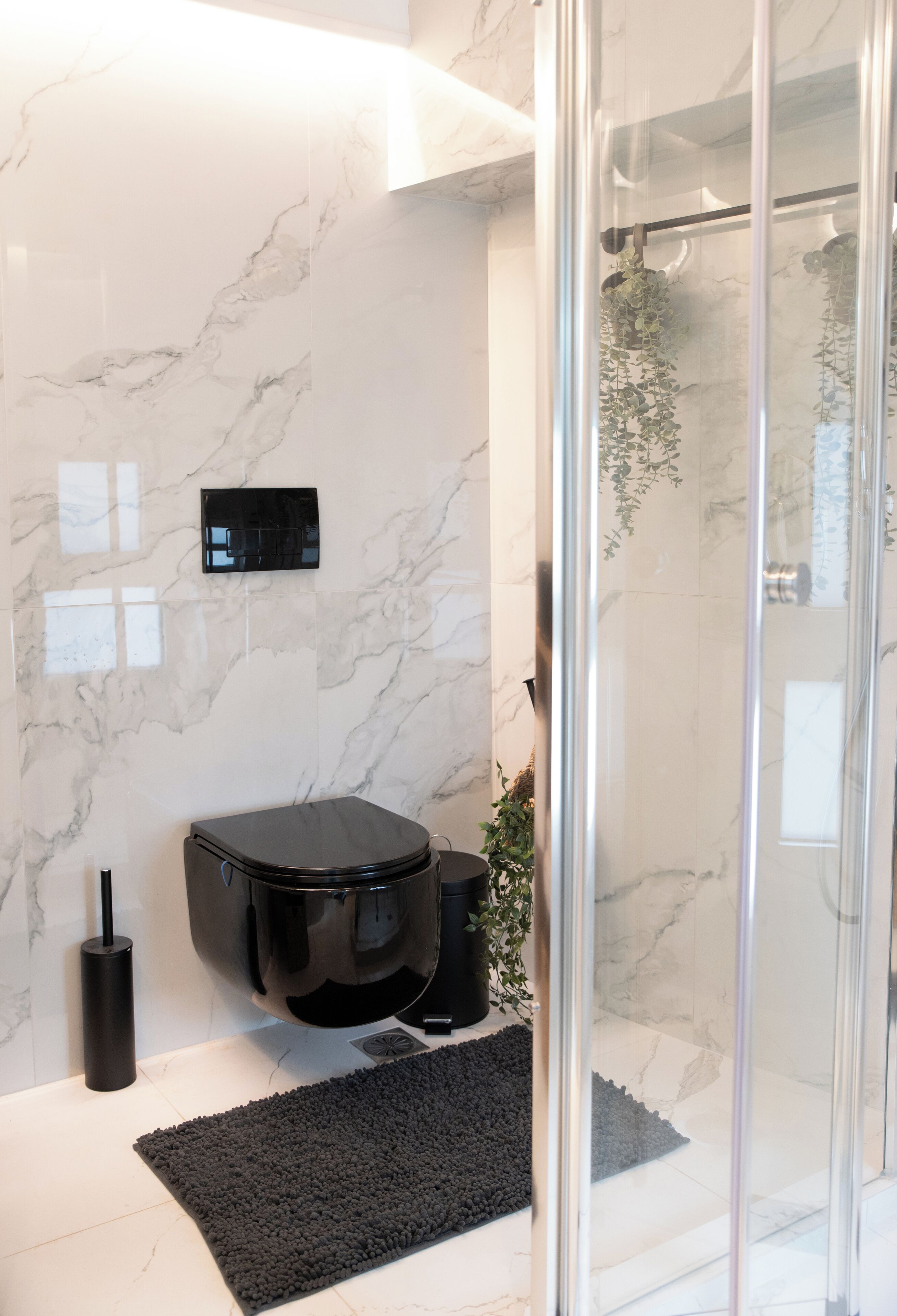 A modern bathroom with a glass shower enclosure, a black toilet, and a marble wall.