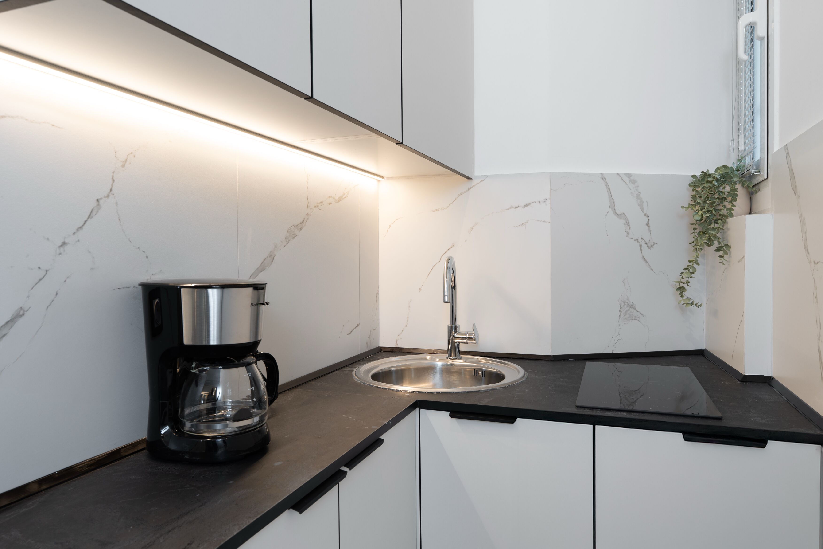 A modern kitchen with white cabinets, a black countertop, a coffee maker, and a sink.