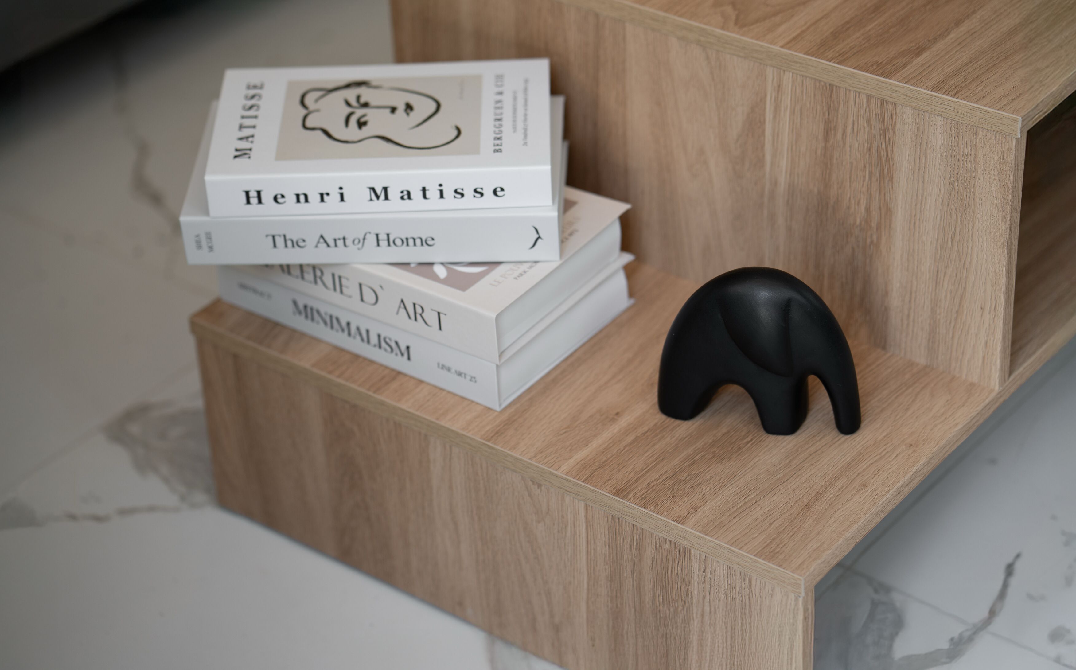 A wooden shelf with a stack of books and a black elephant-shaped object.