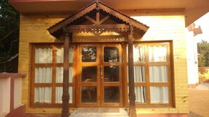A wooden house with a large front door, a porch with a triangular roof, and large windows with curtains. - Baine Holiday Resort (Bolpur)