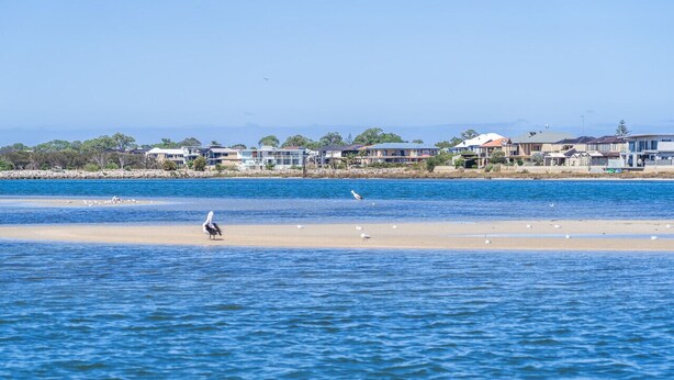A coastal view with a sandy beach and a row of houses in the background.