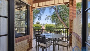 A covered patio with a glass table and chairs, brick walls, and a view of trees and a fence.