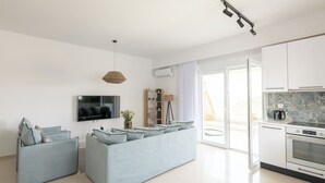 En moderne stue med en grå sofa, et fladskærms-tv og et køkkenområde med komfur og skabe.