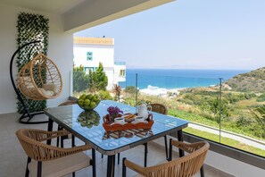 Ein Essbereich mit einem Glastisch, Korbstühlen und Blick aufs Meer.