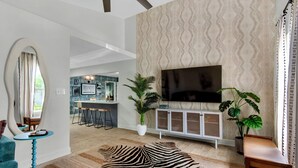 A modern living room with a zebra-patterned rug, a television mounted on a cabinet, and a dining area in the background. - PCB Stay w/ Heated Pool, Hot Tub, Bars, Game Room & Quick Walk to Beach (Panama City Beach)
