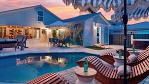 A pool area with wooden loungers, a dining table, and umbrellas. - PCB Stay w/ Heated Pool, Hot Tub, Bars, Game Room & Quick Walk to Beach (Panama City Beach)