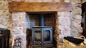 En stenkamin med en vedeldad kamin, en trähylla ovanför och en flätad korg fylld med ved.