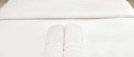 A neatly made bed with white linens and two rolled towels placed at the foot of the bed.